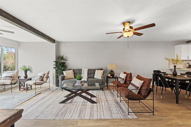 living room with ceiling fan, light hardwood / wood-style flooring, and beamed ceiling