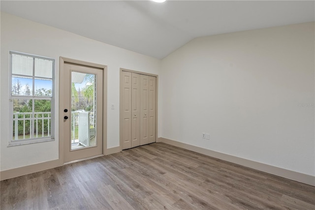 unfurnished bedroom featuring lofted ceiling, access to outside, and light hardwood / wood-style floors