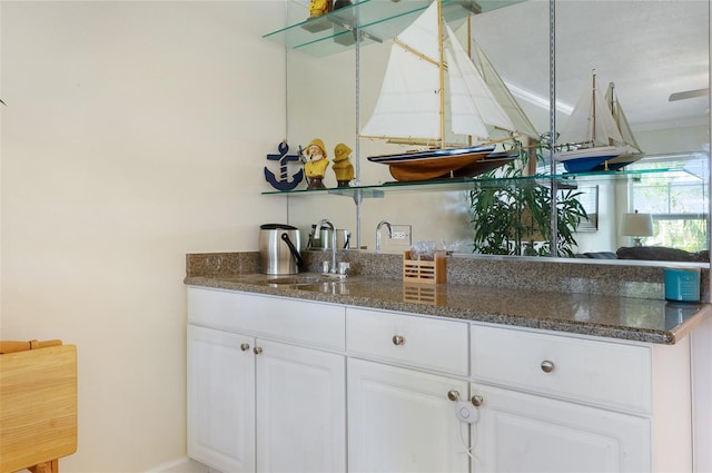 kitchen with crown molding, white cabinets, dark stone counters, and sink