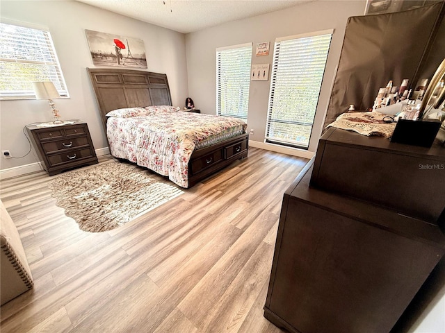 bedroom featuring light hardwood / wood-style flooring, a textured ceiling, and multiple windows