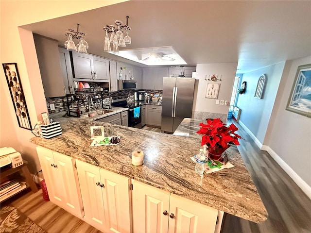 kitchen with appliances with stainless steel finishes, hardwood / wood-style flooring, kitchen peninsula, light stone counters, and gray cabinetry