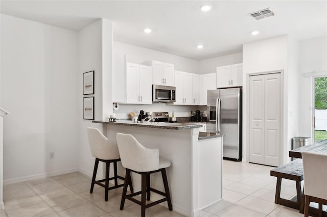 kitchen with a kitchen bar, white cabinetry, stainless steel appliances, dark stone counters, and kitchen peninsula