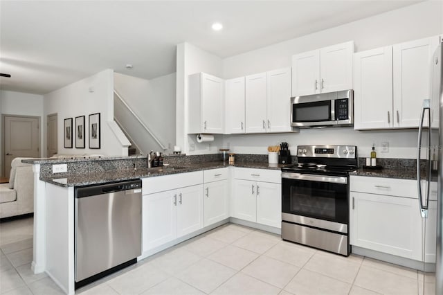 kitchen featuring kitchen peninsula, appliances with stainless steel finishes, light tile patterned flooring, dark stone counters, and white cabinets