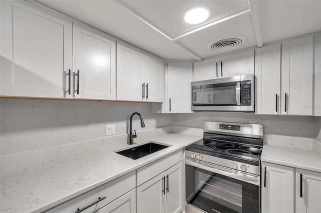 kitchen with stainless steel appliances, white cabinetry, light stone countertops, and sink