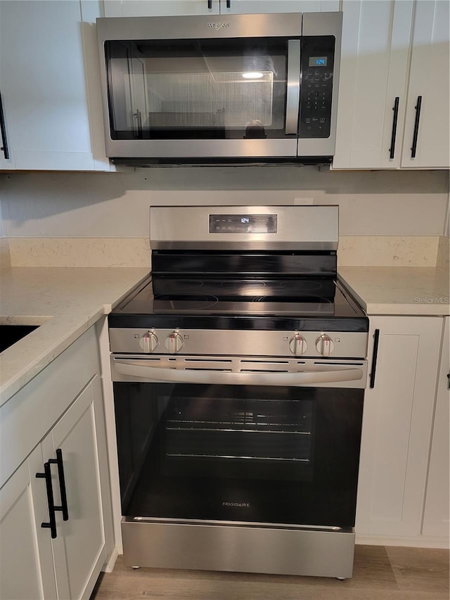 kitchen with light stone counters, stainless steel appliances, light hardwood / wood-style floors, and white cabinets