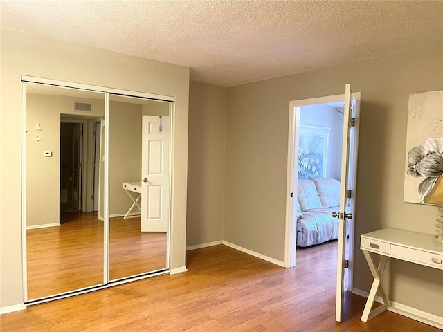 bedroom with light hardwood / wood-style floors, a textured ceiling, and a closet