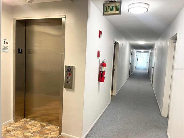 hall featuring a textured ceiling and elevator