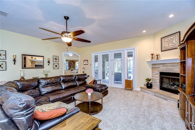 carpeted living room with ceiling fan, a fireplace, a textured ceiling, and french doors