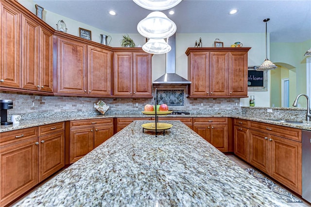 kitchen with sink, tasteful backsplash, light stone counters, decorative light fixtures, and wall chimney range hood