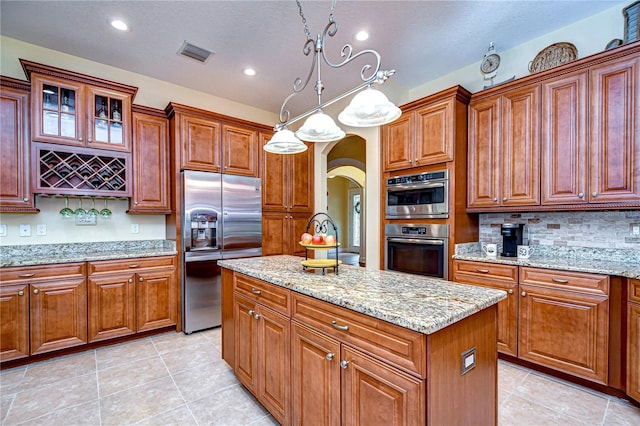 kitchen featuring light tile patterned floors, stainless steel appliances, a center island, light stone counters, and decorative light fixtures