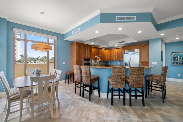 kitchen featuring pendant lighting, kitchen peninsula, a tray ceiling, a breakfast bar area, and stainless steel appliances