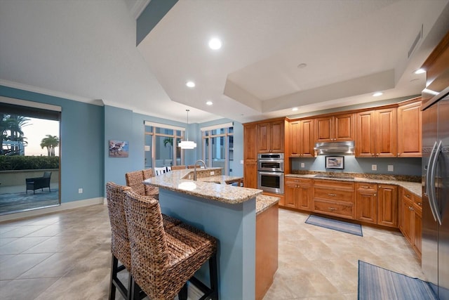 kitchen featuring a breakfast bar area, hanging light fixtures, a center island with sink, and a tray ceiling