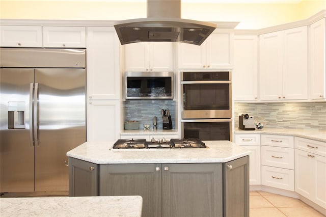 kitchen with island exhaust hood, appliances with stainless steel finishes, tasteful backsplash, light stone countertops, and white cabinets