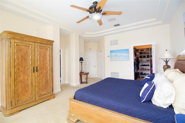 bedroom featuring a walk in closet, a closet, ceiling fan, light colored carpet, and a tray ceiling