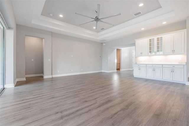 unfurnished living room with light hardwood / wood-style floors, ceiling fan, and a raised ceiling