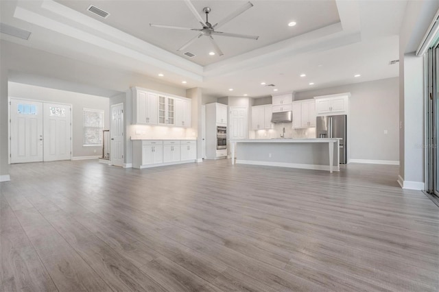 unfurnished living room with sink, ceiling fan, a raised ceiling, and light hardwood / wood-style flooring