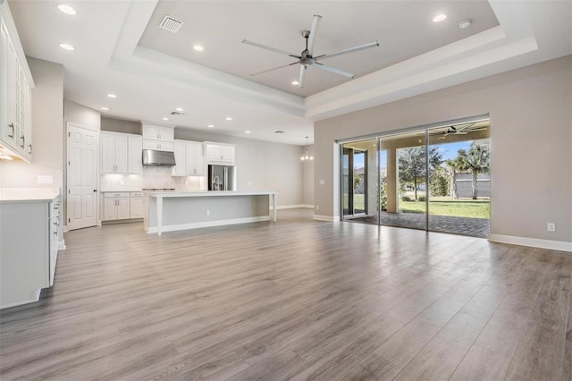 unfurnished living room with light hardwood / wood-style floors, a tray ceiling, and ceiling fan