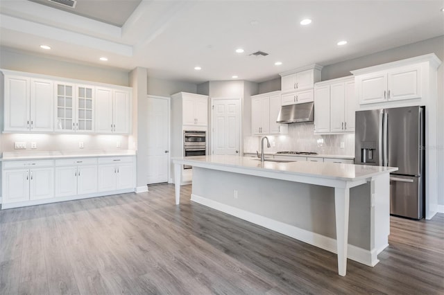 kitchen with white cabinetry, stainless steel appliances, sink, light wood-type flooring, and a center island with sink