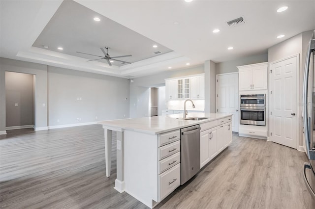 kitchen with white cabinetry, appliances with stainless steel finishes, a center island with sink, and a raised ceiling