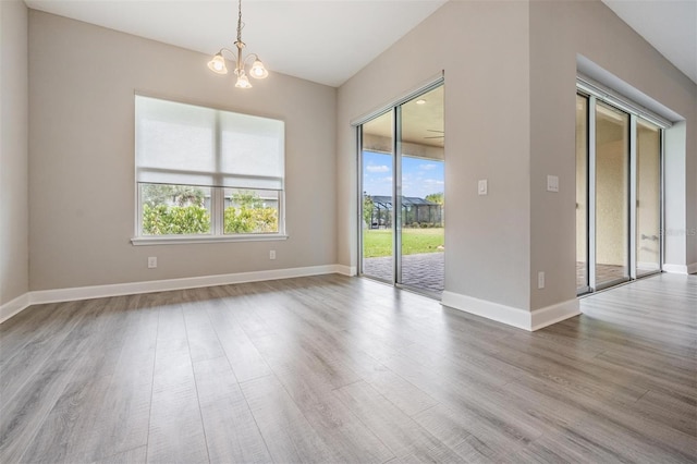 empty room with a notable chandelier, a healthy amount of sunlight, and wood-type flooring