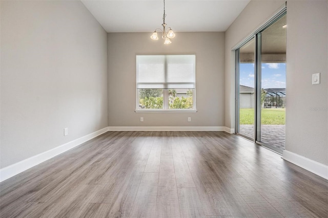 empty room with hardwood / wood-style flooring, a notable chandelier, and a healthy amount of sunlight