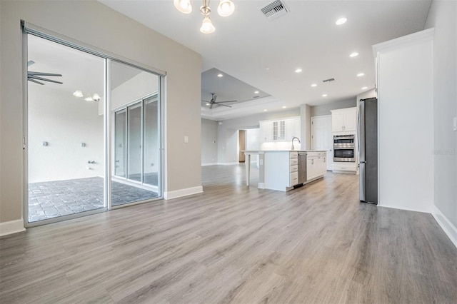 unfurnished living room featuring sink, light hardwood / wood-style floors, ceiling fan, and a raised ceiling