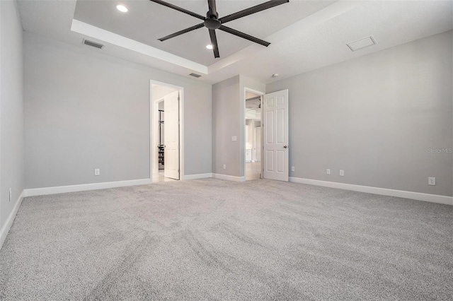 empty room featuring ceiling fan, a raised ceiling, and carpet floors