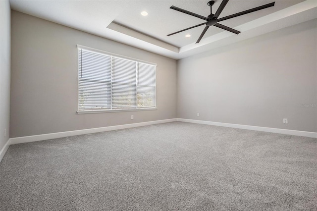 empty room with carpet floors, ceiling fan, and a raised ceiling