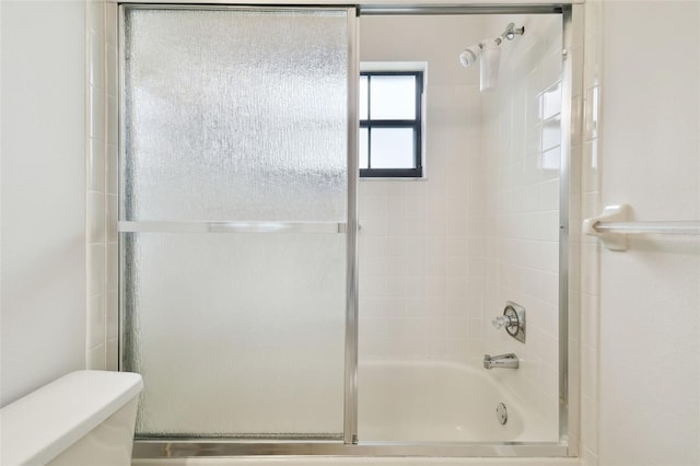 bathroom featuring toilet and shower / bath combination with glass door