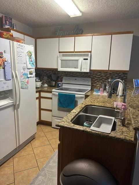 kitchen featuring sink, white appliances, white cabinetry, light tile patterned flooring, and a textured ceiling