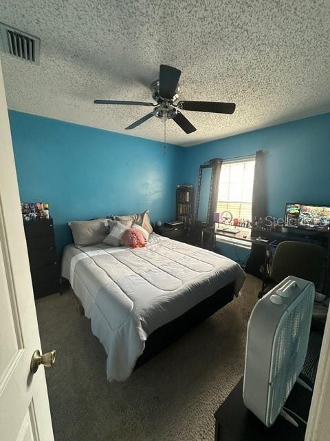 bedroom featuring ceiling fan, a textured ceiling, and dark colored carpet