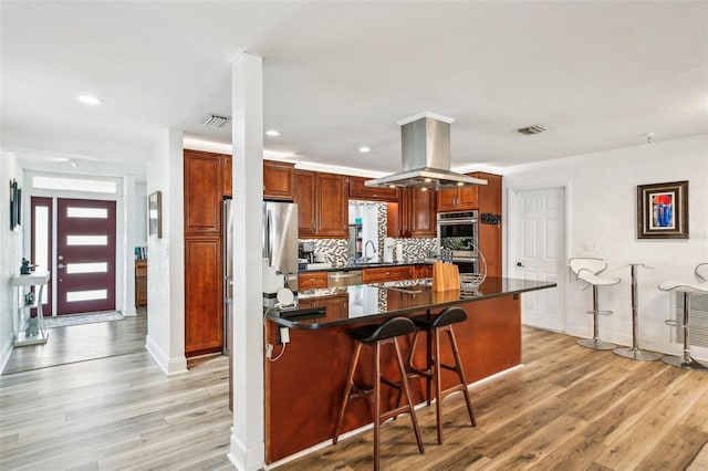 kitchen featuring decorative backsplash, light wood-type flooring, a kitchen breakfast bar, stainless steel appliances, and island range hood