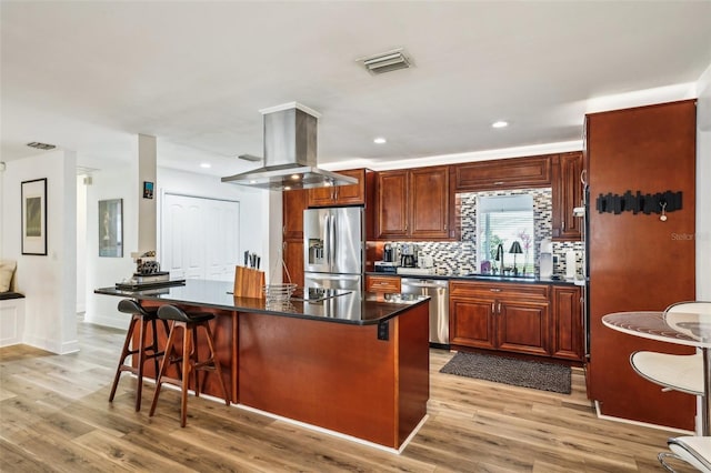 kitchen featuring island exhaust hood, stainless steel appliances, a kitchen breakfast bar, a kitchen island, and sink