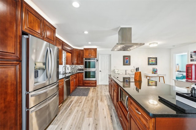 kitchen featuring tasteful backsplash, light hardwood / wood-style floors, stainless steel appliances, dark stone counters, and island range hood