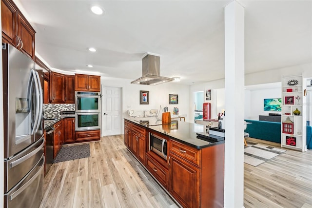 kitchen featuring dark stone countertops, light hardwood / wood-style floors, decorative backsplash, island exhaust hood, and appliances with stainless steel finishes