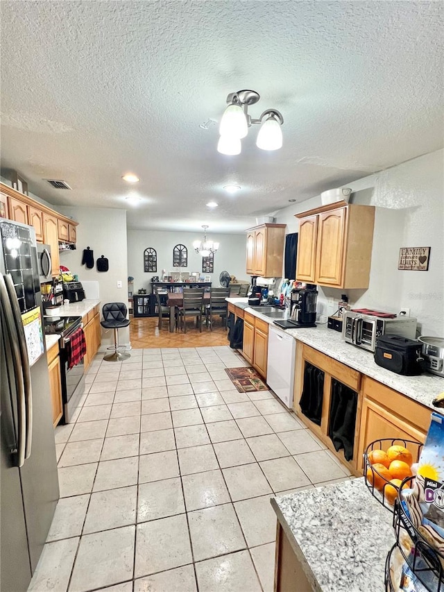 kitchen with light tile patterned floors, a textured ceiling, a chandelier, and appliances with stainless steel finishes