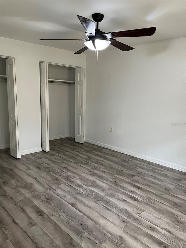unfurnished bedroom featuring ceiling fan, baseboards, multiple closets, and dark wood finished floors