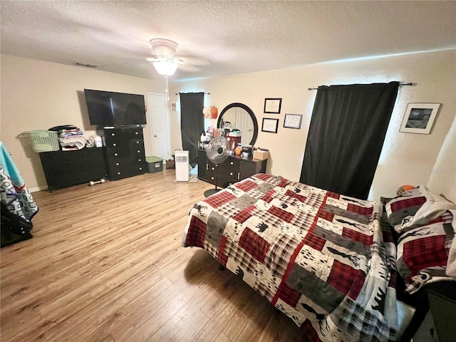 bedroom with ceiling fan, visible vents, a textured ceiling, and wood finished floors