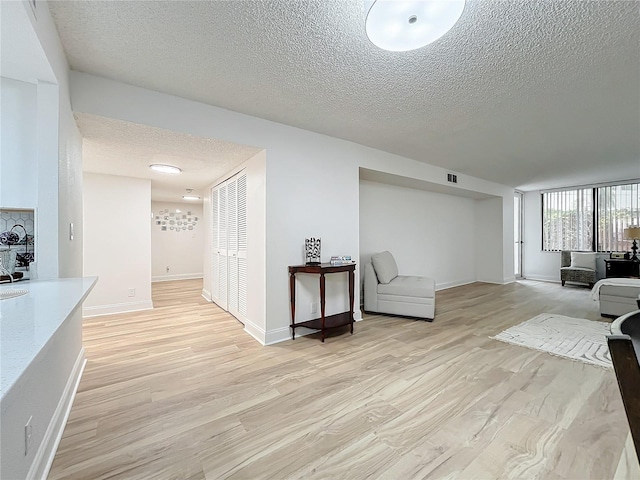 interior space featuring a textured ceiling, baseboards, visible vents, and light wood-style floors