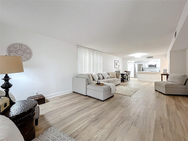 living area with a textured ceiling, visible vents, light wood-style flooring, and baseboards