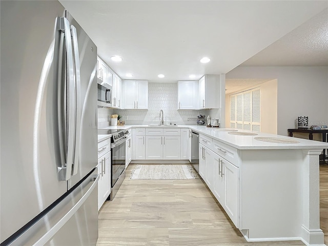 kitchen featuring a peninsula, a sink, light countertops, appliances with stainless steel finishes, and decorative backsplash