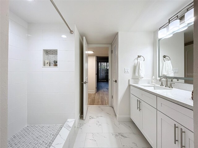 bathroom with marble finish floor, baseboards, a tile shower, and vanity