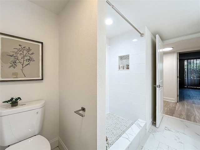 bathroom with marble finish floor, baseboards, a tile shower, and toilet