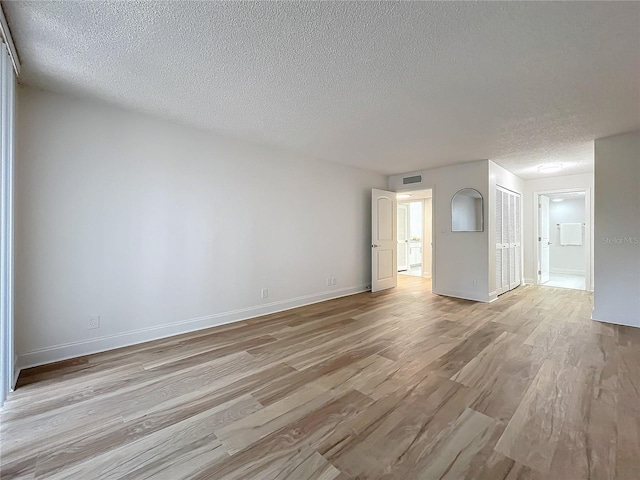 spare room with light wood finished floors, baseboards, visible vents, and a textured ceiling