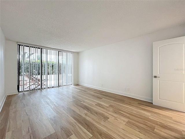 empty room with light wood-type flooring, a textured ceiling, and baseboards