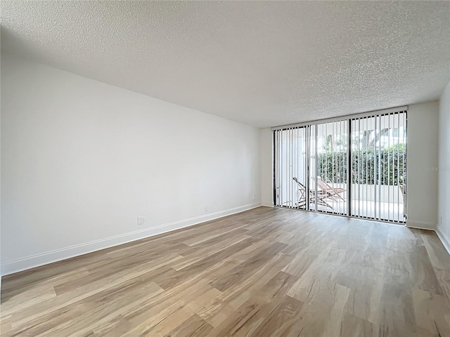 unfurnished room with light wood-style floors, floor to ceiling windows, baseboards, and a textured ceiling