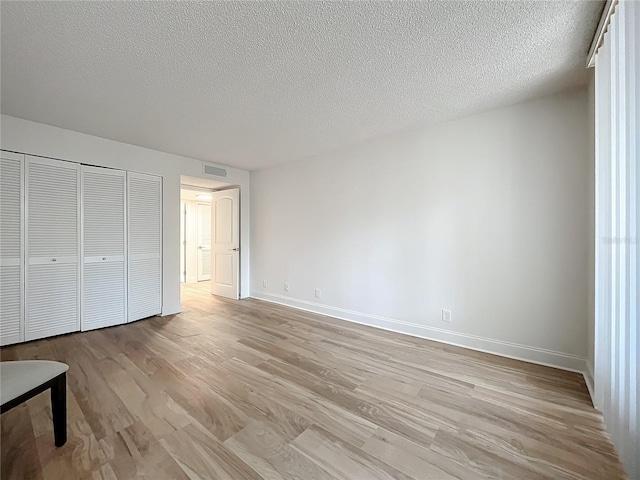 unfurnished bedroom featuring light wood-style floors, baseboards, visible vents, and a textured ceiling