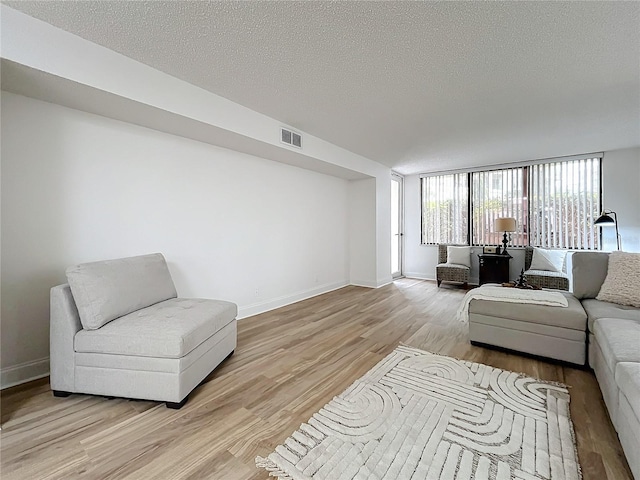 living area with light wood finished floors, baseboards, visible vents, and a textured ceiling