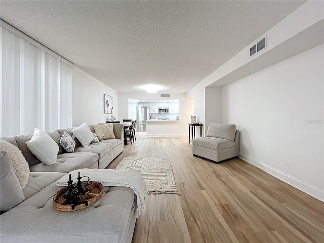 living room featuring a textured ceiling, light wood-type flooring, visible vents, and baseboards