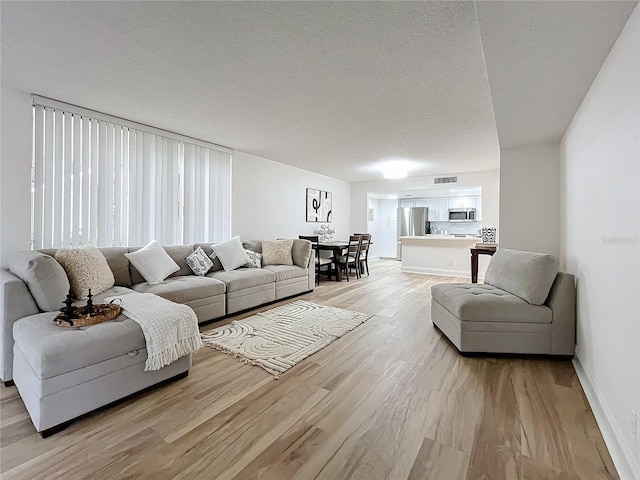 living area with a textured ceiling, light wood finished floors, visible vents, and baseboards